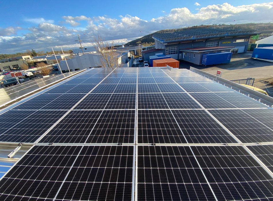 Große Photovoltaikanlage auf einem Gewerbedach mit Berglandschaft im Hintergrund