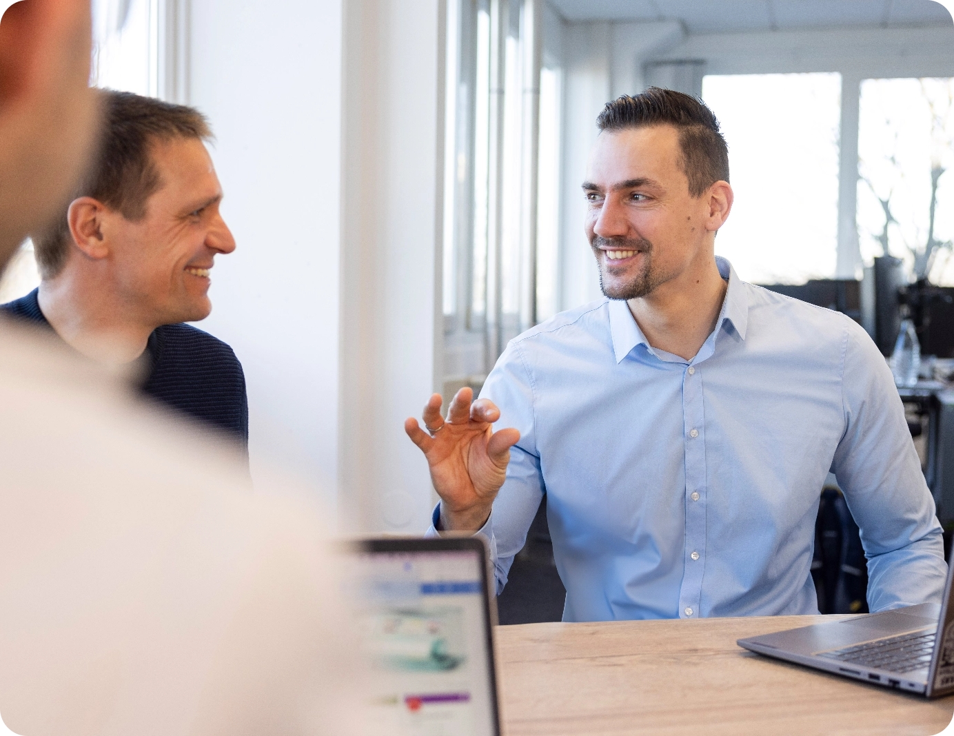 Energieberatung bei SymbioGrid Zwei Mitarbeiter in einem Business-Meeting, gestikulierend im Gespräch über Energielösungen